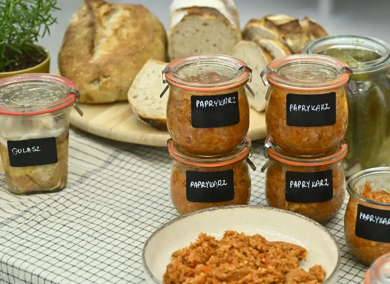 Słoiki z paprykarzem i gulaszem, jak u babci. Obok świeże pieczywo i ogórki.