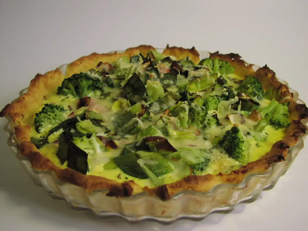 En gyllene broccoli och &auml;delostpaj med en krispig botten, fylld med gr&ouml;na broccolibuketter och purjol&ouml;k i en kr&auml;mig &auml;delosts&aring;s.
