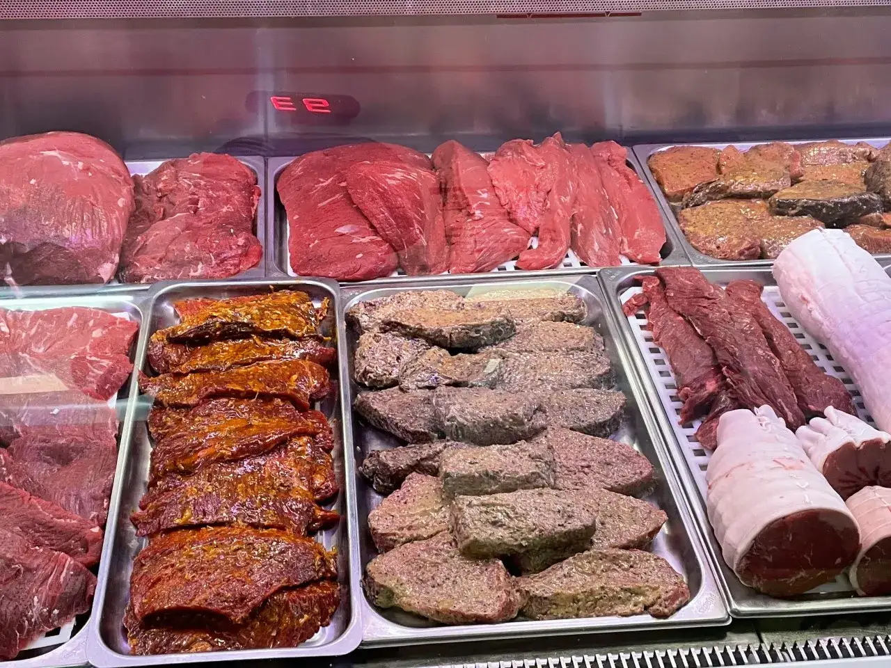 Vitrine de boucherie présentant divers types de viande rouge : steaks marinés, brochettes, rôtis et pièces de bœuf.