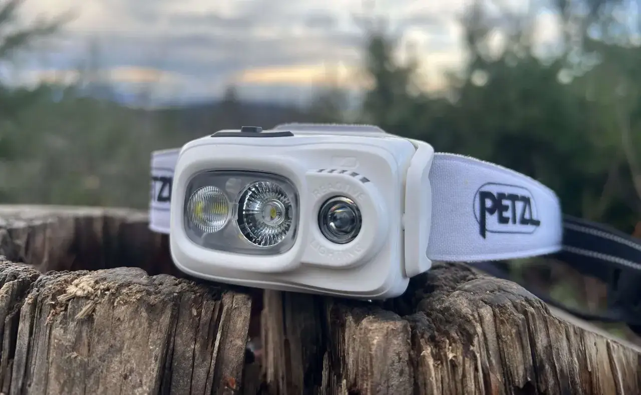 Petzl Swift RL im Test: Eine wei&szlig;e Stirnlampe mit zwei Leuchten und dem Petzl-Logo auf dem Band, platziert auf einem Baumstumpf im Freien.