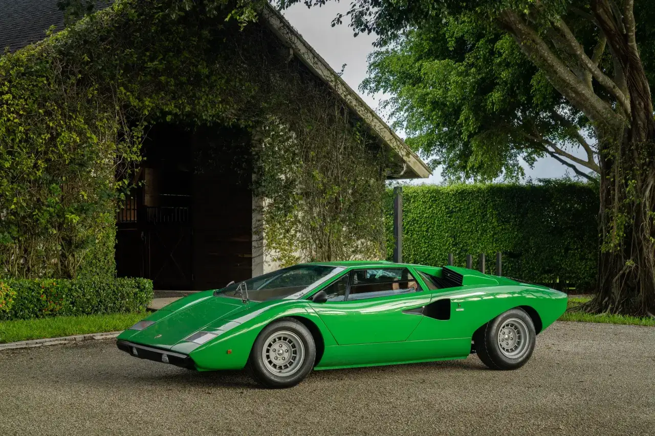 Gr&uuml;ner Lamborghini Countach LP400, ein ikonischer Sportwagen, parkt vor einem von Pflanzen &uuml;berwucherten Geb&auml;ude.