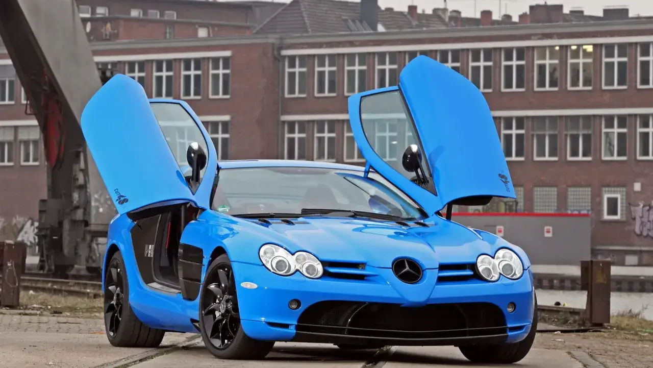 Niebieski Mercedes McLaren z otwartymi drzwiami, gotowy do jazdy po industrialnym terenie.