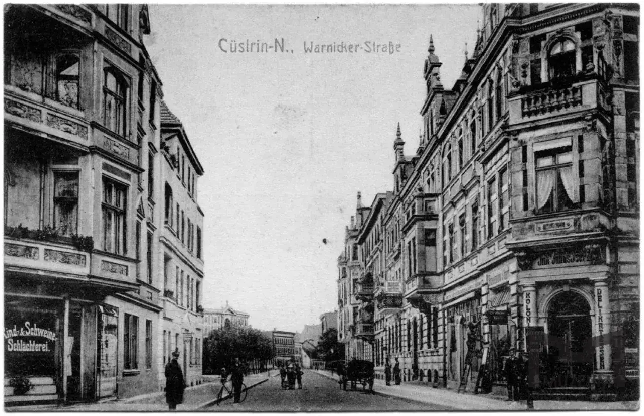 Ulica Warnicka w Kostrzynie nad Odrą przed wojną. Kamienice, sklep mięsny i dorożka na brukowanej ulicy.
