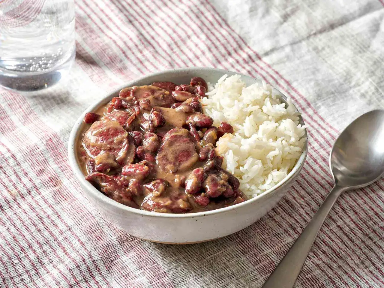 Un bol de riz blanc à côté d'une préparation de cuisson haricots rouges avec des saucisses.