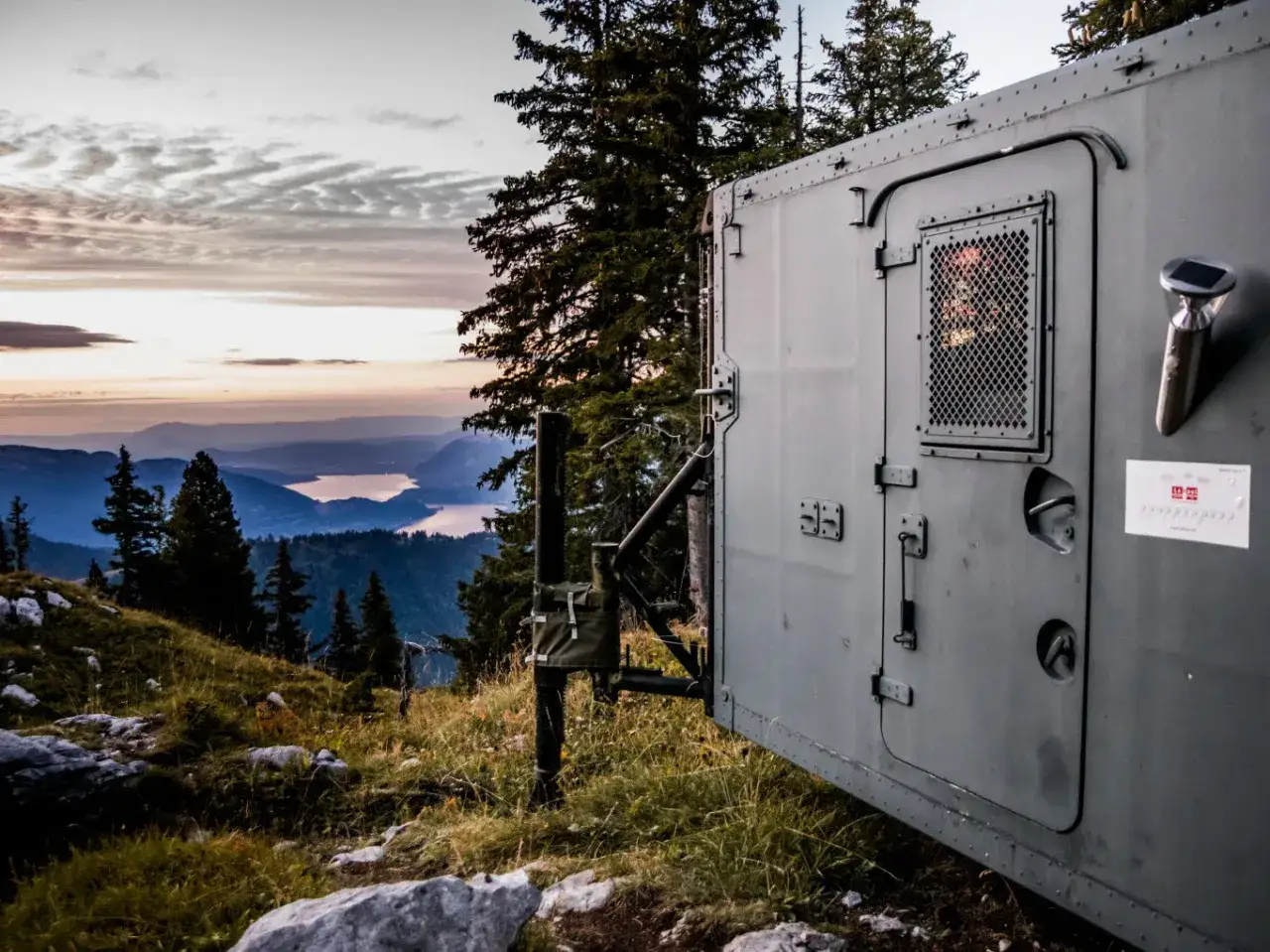 Vue d'une cabane en Haute-Savoie, perchée sur une colline avec un lac en contrebas. Le ciel au crépuscule est nuageux.