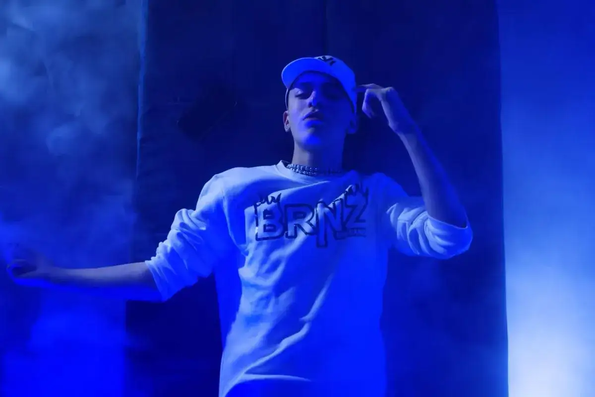 Un giovane skinny cantante con un cappellino bianco e una felpa con la scritta