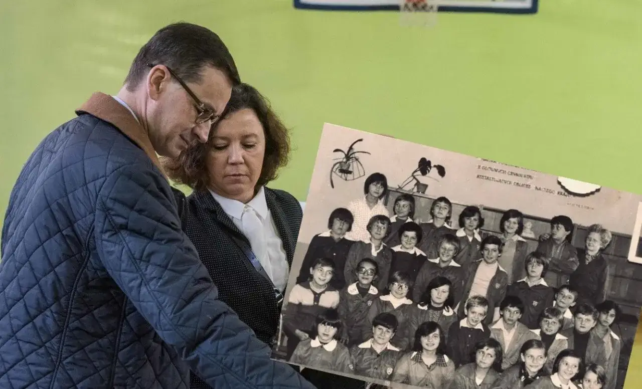Mateusz Morawiecki z żoną oglądają stare zdjęcie z dziećmi w wieku szkolnym.