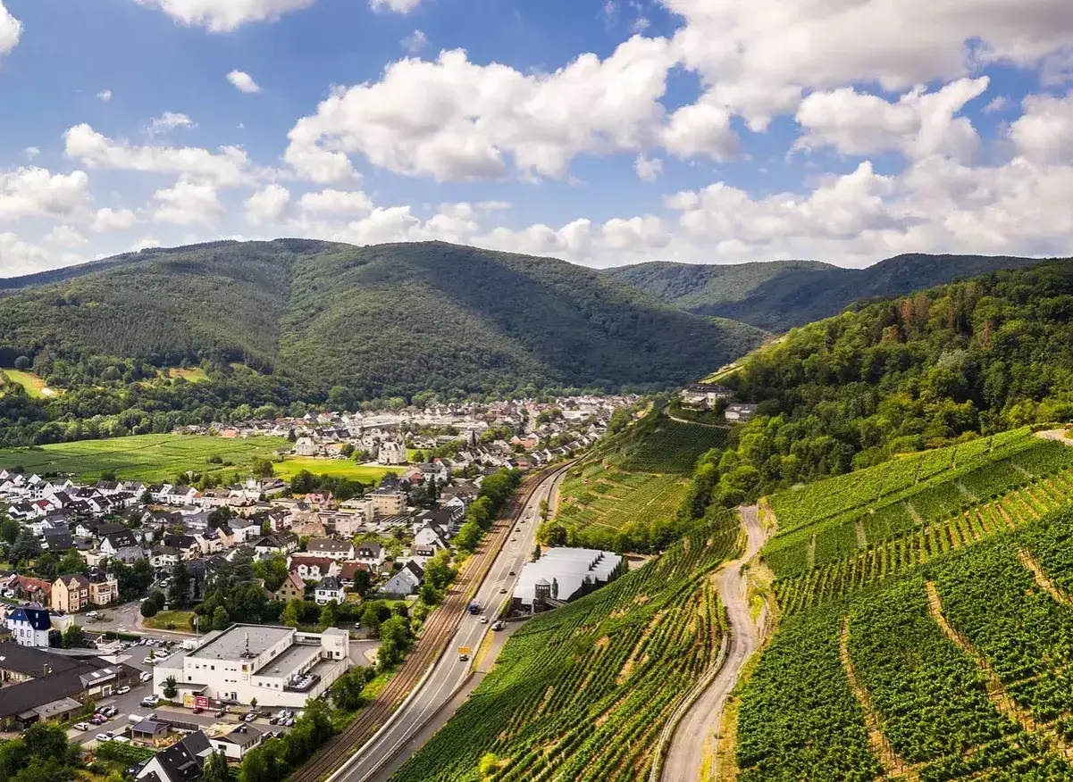 Blick &uuml;ber eine malerische weinregion in der Eifel mit steilen Weinbergen, einem Dorf und einer Stra&szlig;e.