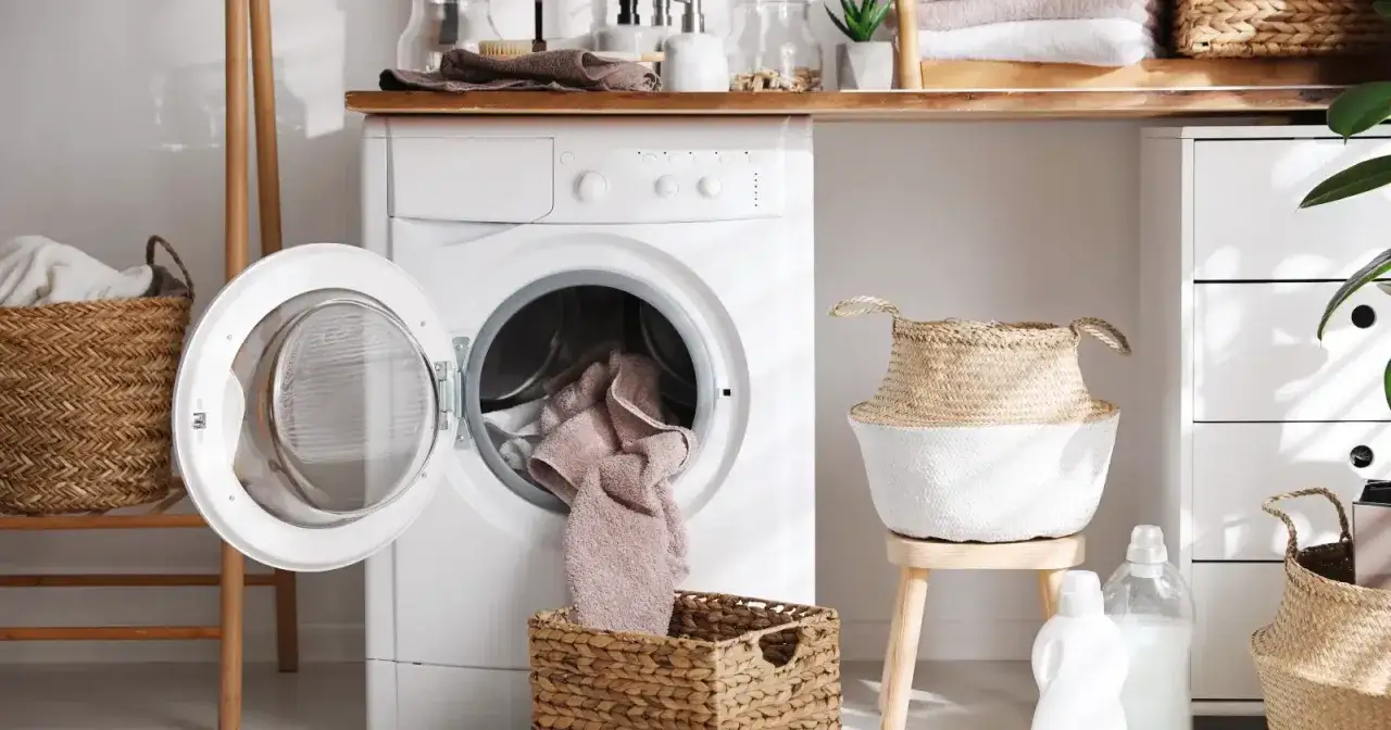 Pralka nie pobiera wody, a ręcznik wypada z bębna. W tle kosze na pranie i akcesoria łazienkowe.