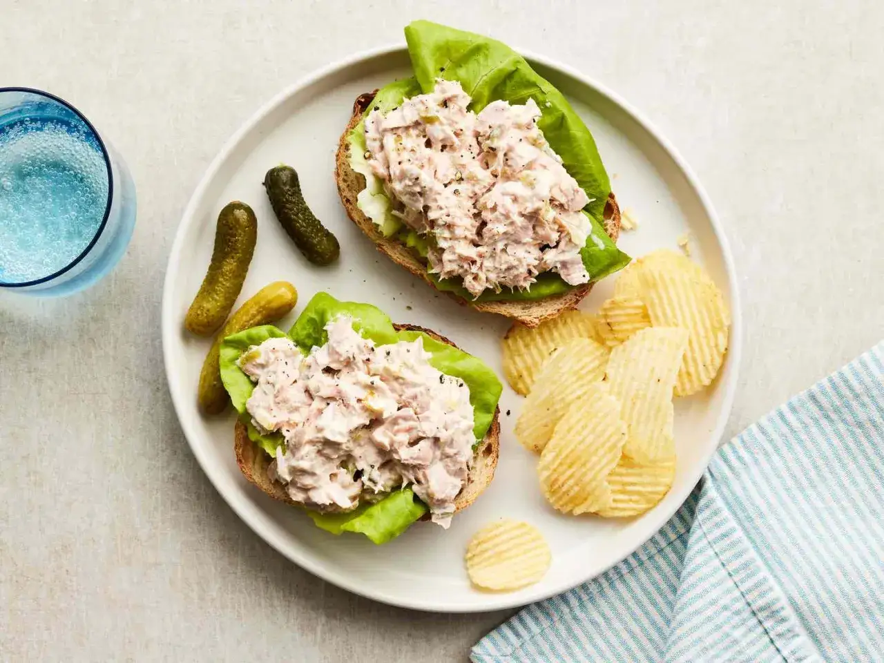 Zwei offene Sandwiches mit Thunfischsalat auf Salatblatt und Vollkornbrot, dazu Cornichons und Kartoffelchips. Perfekt f&uuml;r schnelle Thunfisch Rezepte.