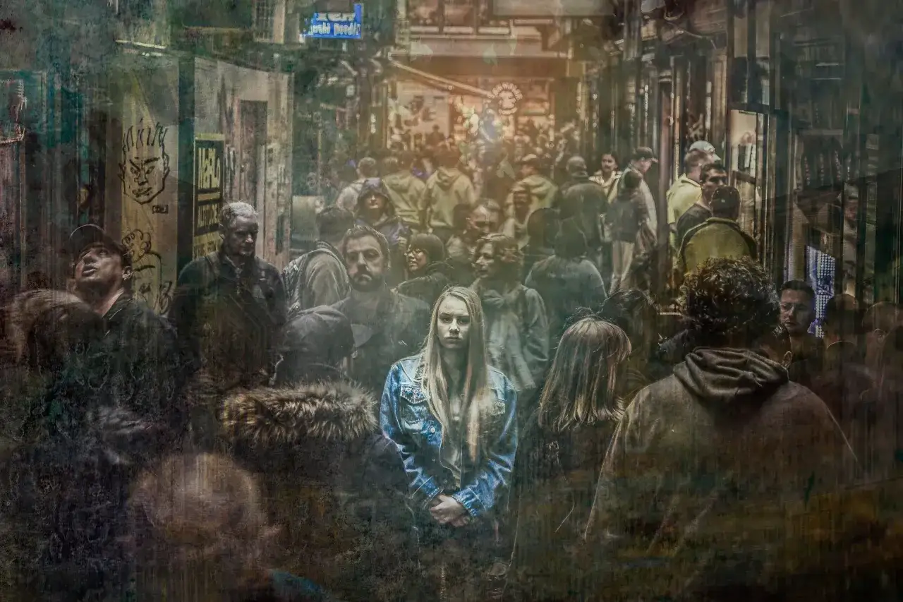 Młoda kobieta w dżinsowej kurtce pośród tłumu, jej wyraz twarzy sugeruje motyw cierpienia.
