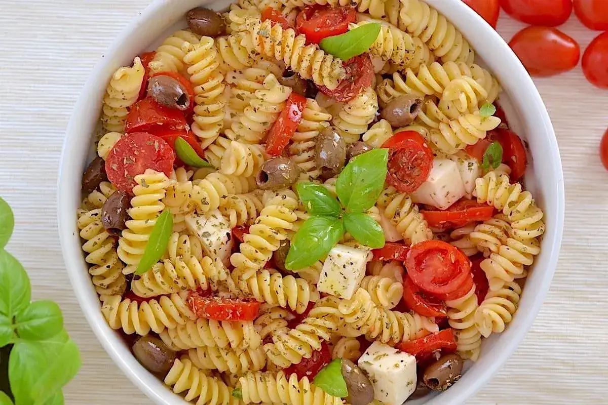 Insalata di pasta vegetariana con fusilli, pomodorini, olive, mozzarella e basilico fresco. Un piatto colorato e gustoso.