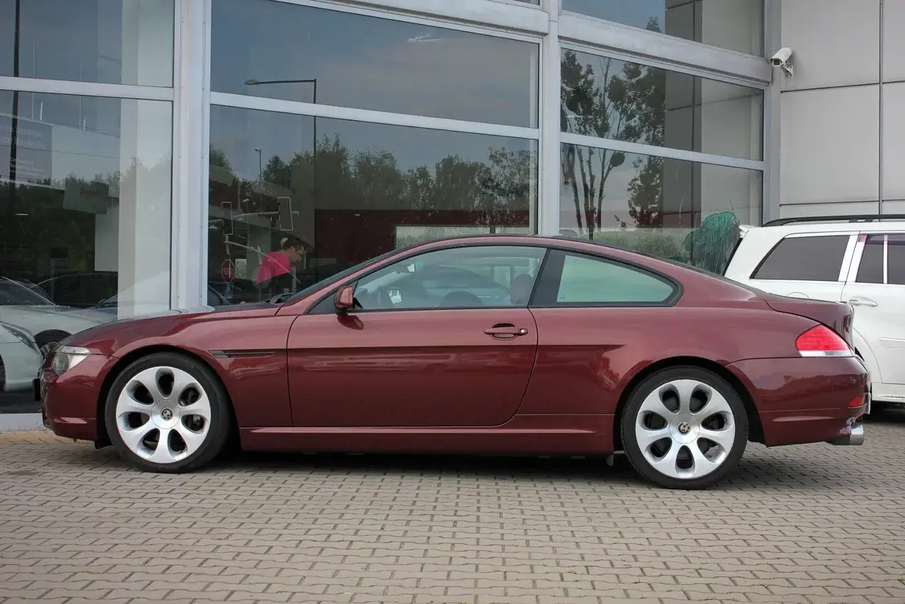 Eleganckie, bordowe BMW E63 coupe z charakterystycznymi felgami stoi przed salonem samochodowym.
