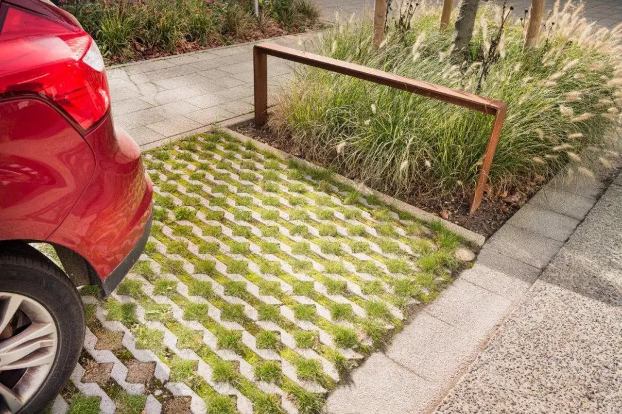 Une voiture rouge est gar&eacute;e sur une all&eacute;e de garage drainante avec de l'herbe poussant entre les dalles.