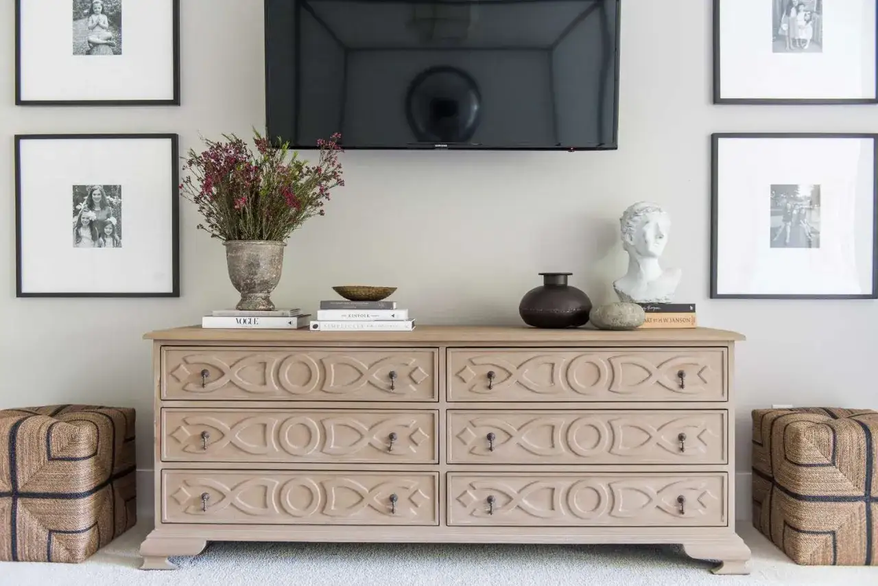 Comò in legno chiaro con decorazioni geometriche, ideale per la camera da letto. Sopra, vasi, libri e busto.