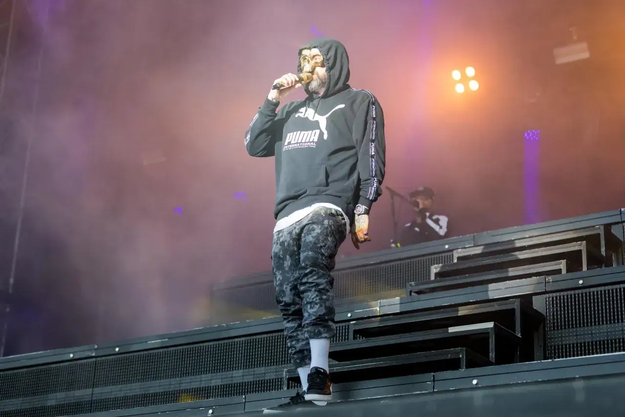 Rapper mit Totenkopfmaske und Puma-Hoodie auf Bühne. So sieht was ist rap aus: ein Mann, der seine Worte in die Menge schleudert.