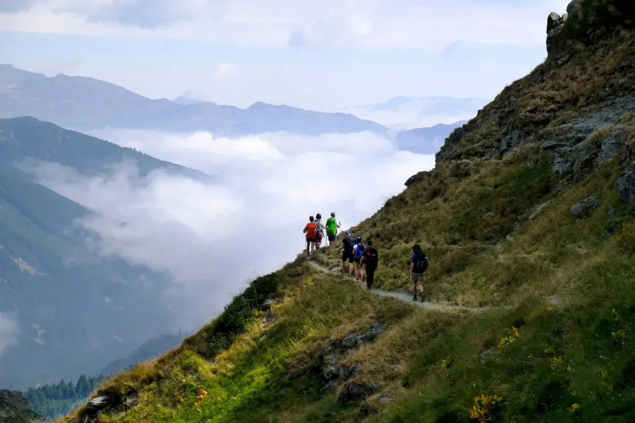Senderismo por las montañas malditas de Albania, con excursionistas en un sendero estrecho sobre un mar de nubes.