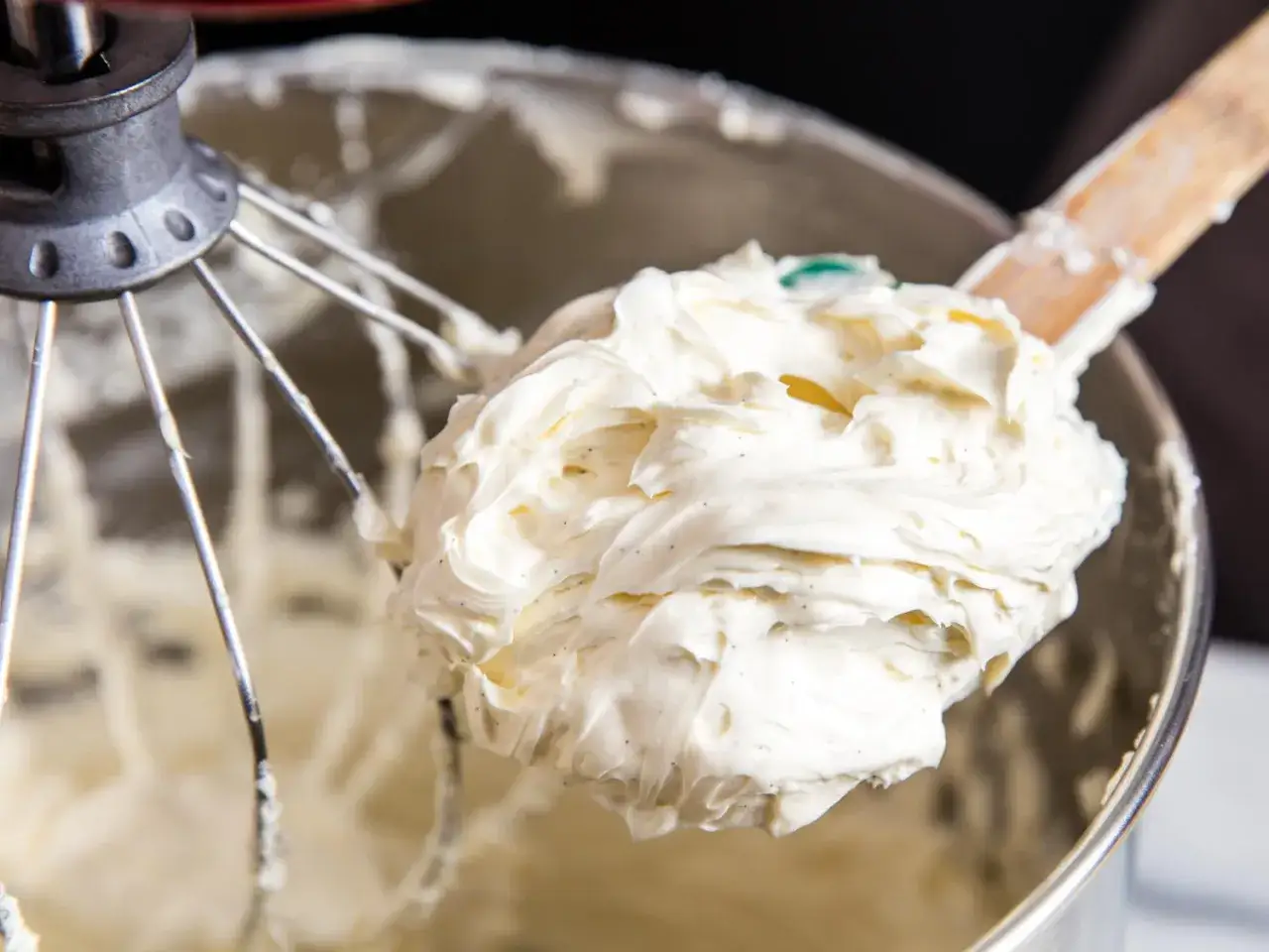 Cremige swiss meringue buttercreme mit Vanillepunkten, auf einem Holzlöffel in einer Rührschüssel.