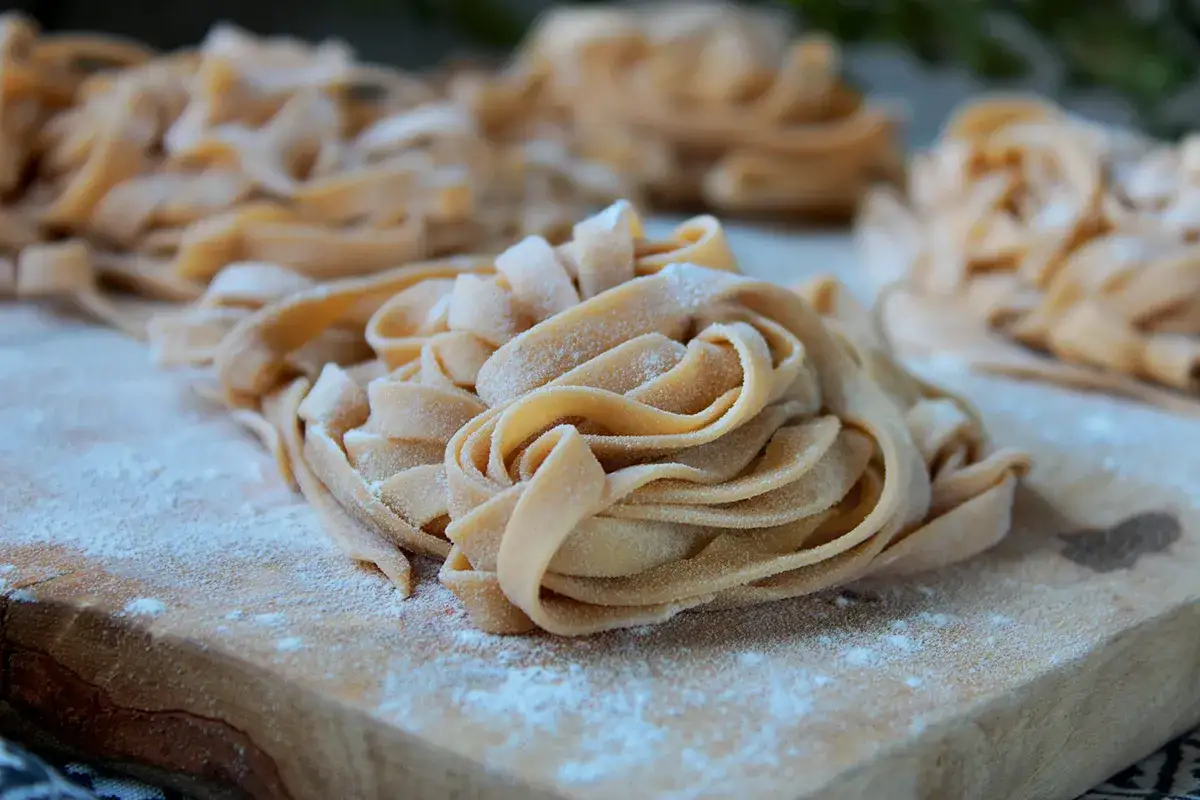 Świeży, domowy makaron tagliatelle na desce, posypany mąką. Idealny przepis, jak zrobić makaron.