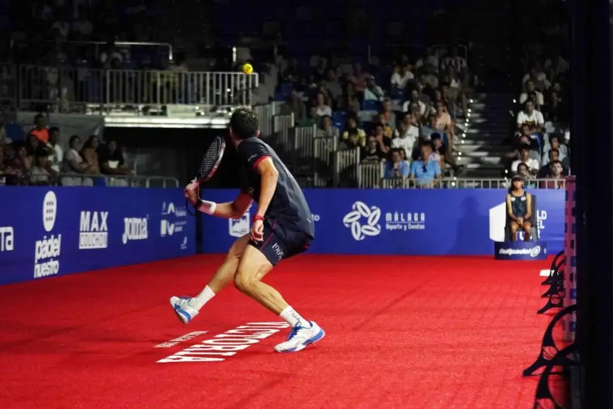Giocatore di padel in azione, con un potente colpo che colpisce la palla gialla. Pubblico sugli spalti.