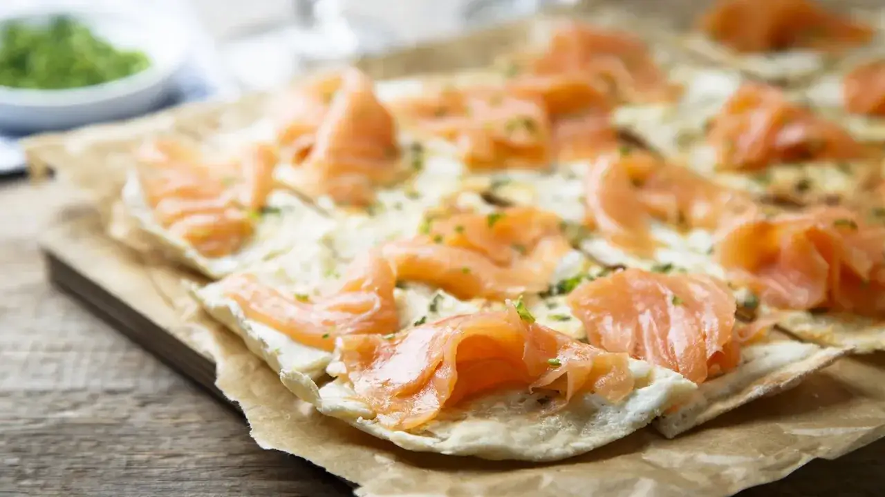 Dünner Flammkuchen mit zartem Lachs belegt, bestreut mit Kräutern. Ein Genuss für Augen und Gaumen.