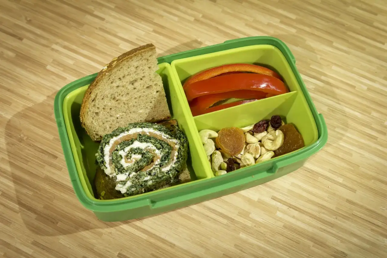 Zielony lunchbox z pieczywem, roladką ze szpinakiem i łososiem, papryką, orzechami i suszonymi owocami. Inspiracja na lunchbox do pracy przepisy.