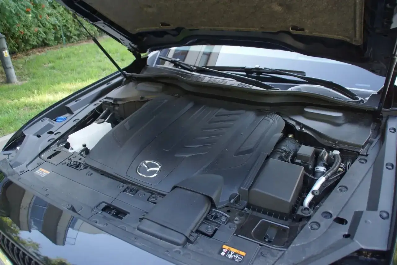 Silnik Mazdy CX-60 3.3 diesel pod otwartą maską. Widoczny czarny, plastikowy cover silnika z logo Mazdy.