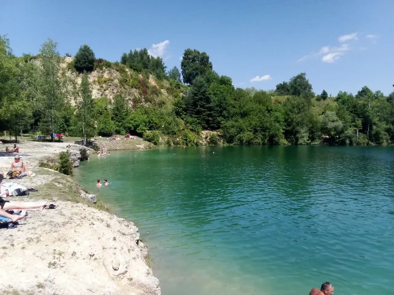 Słoneczny dzień nad zalewem Balaton Trzebinia. Ludzie odpoczywają na brzegu i kąpią się w turkusowej wodzie.