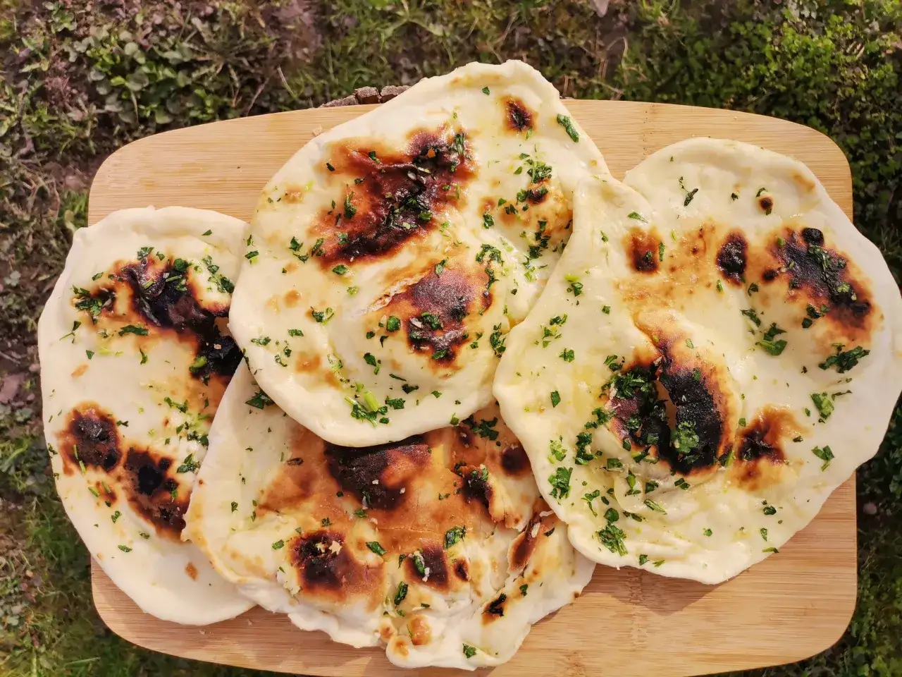 Pyszny, świeżo upieczony chlebek naan, posypany zieloną pietruszką, leży na drewnianej desce. Idealny do curry!