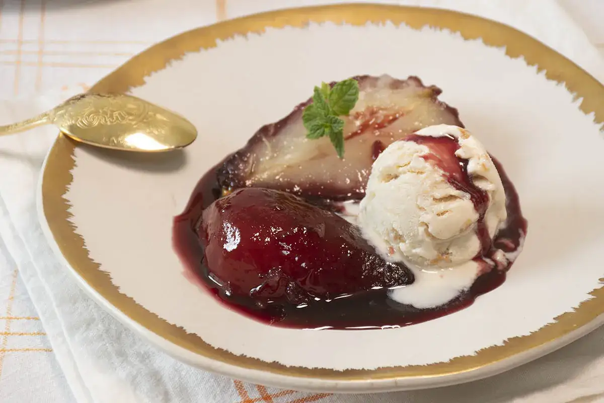 Peras al vino, tiernas y brillantes, acompa&ntilde;adas de helado cremoso y una hoja de menta. Un postre elegante.