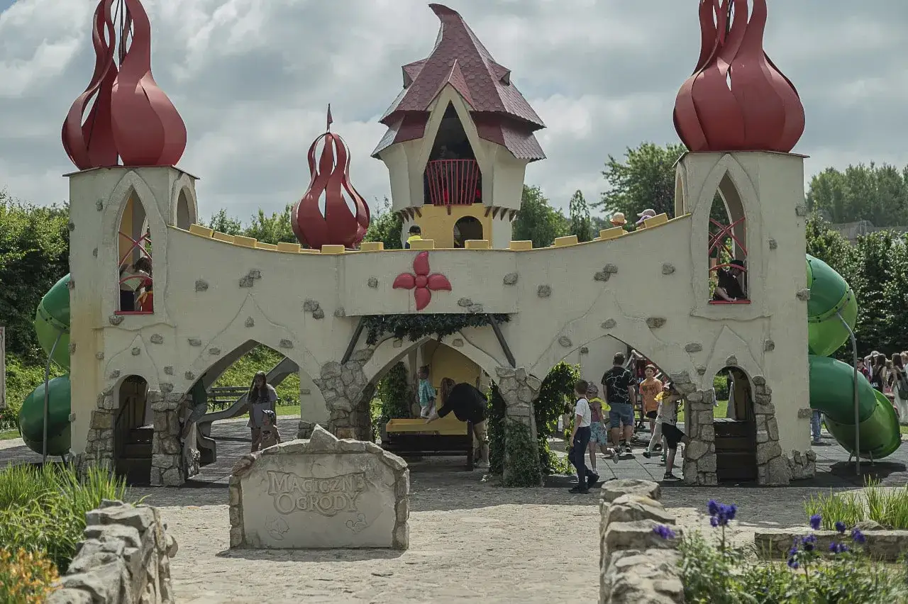 Dzieci bawią się w zamku, kt&oacute;ry jest częścią magiczne ogrody atrakcje. Zielone zjeżdżalnie i czerwone wieżyczki dodają mu bajkowego charakteru.