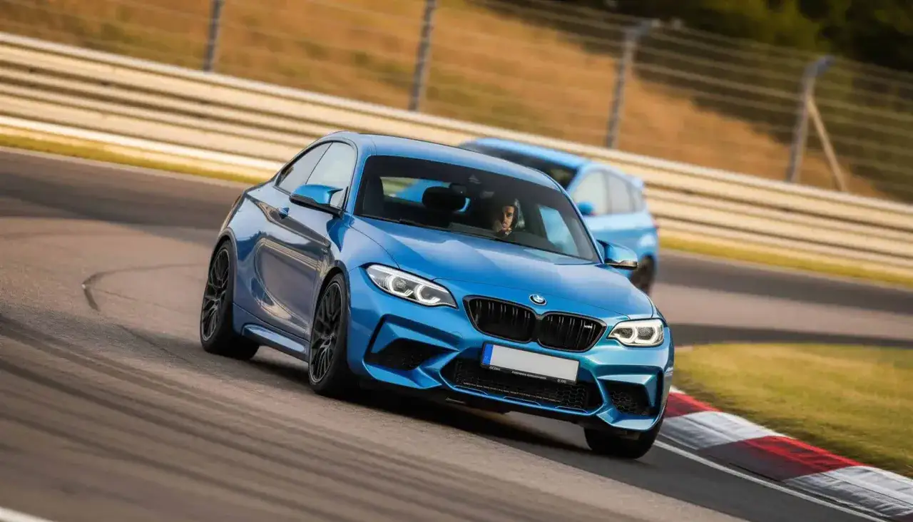 Blauer BMW M2 Competition auf Rennstrecke, Fahrer im Fokus, dynamische Kurvenfahrt.