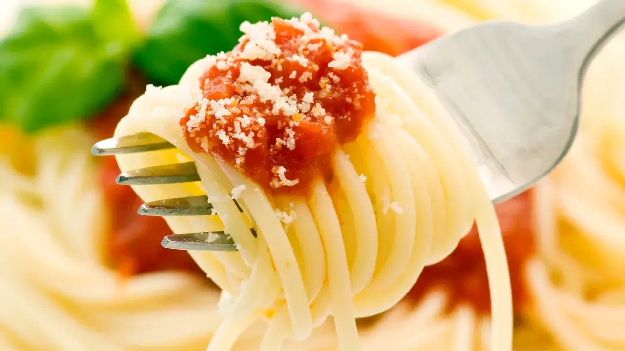 Widok z bliska na widelec z makaronem spaghetti polanym sosem pomidorowym i posypanym parmezanem. Idealny przykład, ile się gotuje makaron, by był al dente.