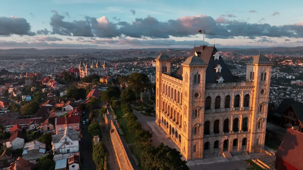 Zachód słońca nad malowniczym miastem na Madagaskarze. W oddali widać rozległą panoramę zabudowań, a na pierwszym planie majestatyczny pałac.