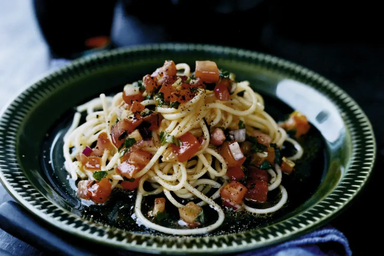Enkel pasta med färska tomater och örter på en mörkgrön tallrik. En snabb och god måltid.