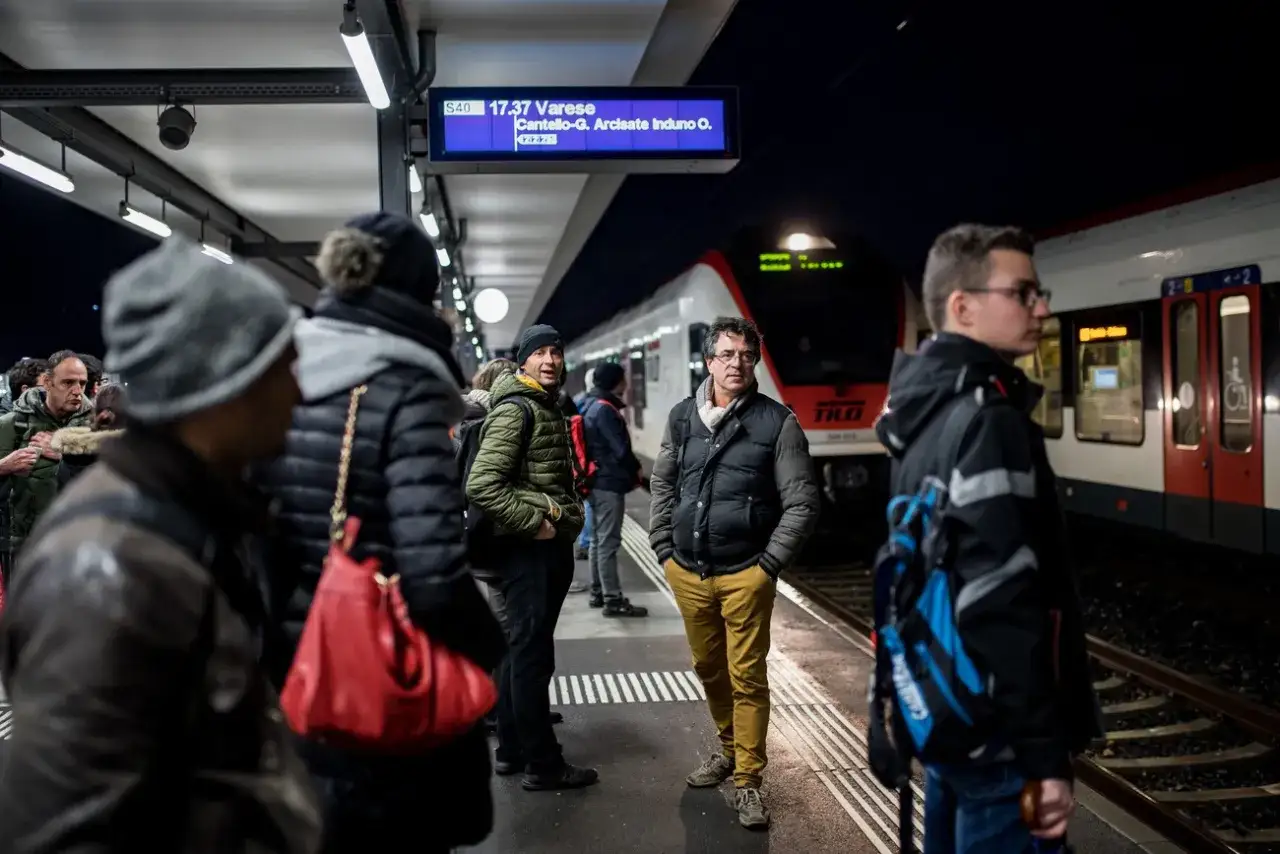 Persone in attesa su una banchina ferroviaria, con un treno in arrivo. Forse stanno tornando a casa dopo una giornata di lavoro, perch&eacute; lavorare in Svizzera conviene.