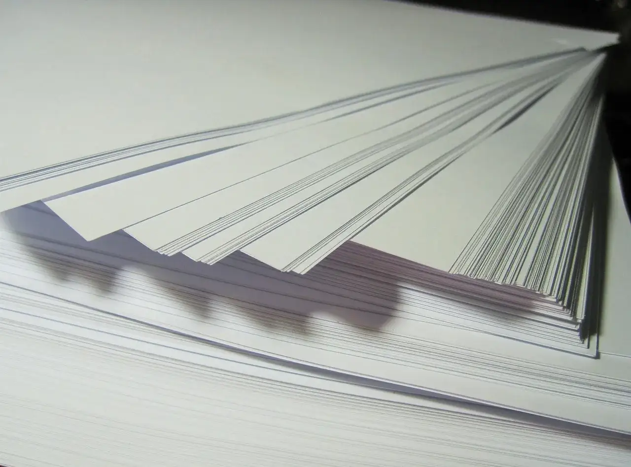 Stos białych kartek, idealnych jako papier fotograficzny do drukarki atramentowej. Wybierz najlepszy papier do swoich wydruk&oacute;w.