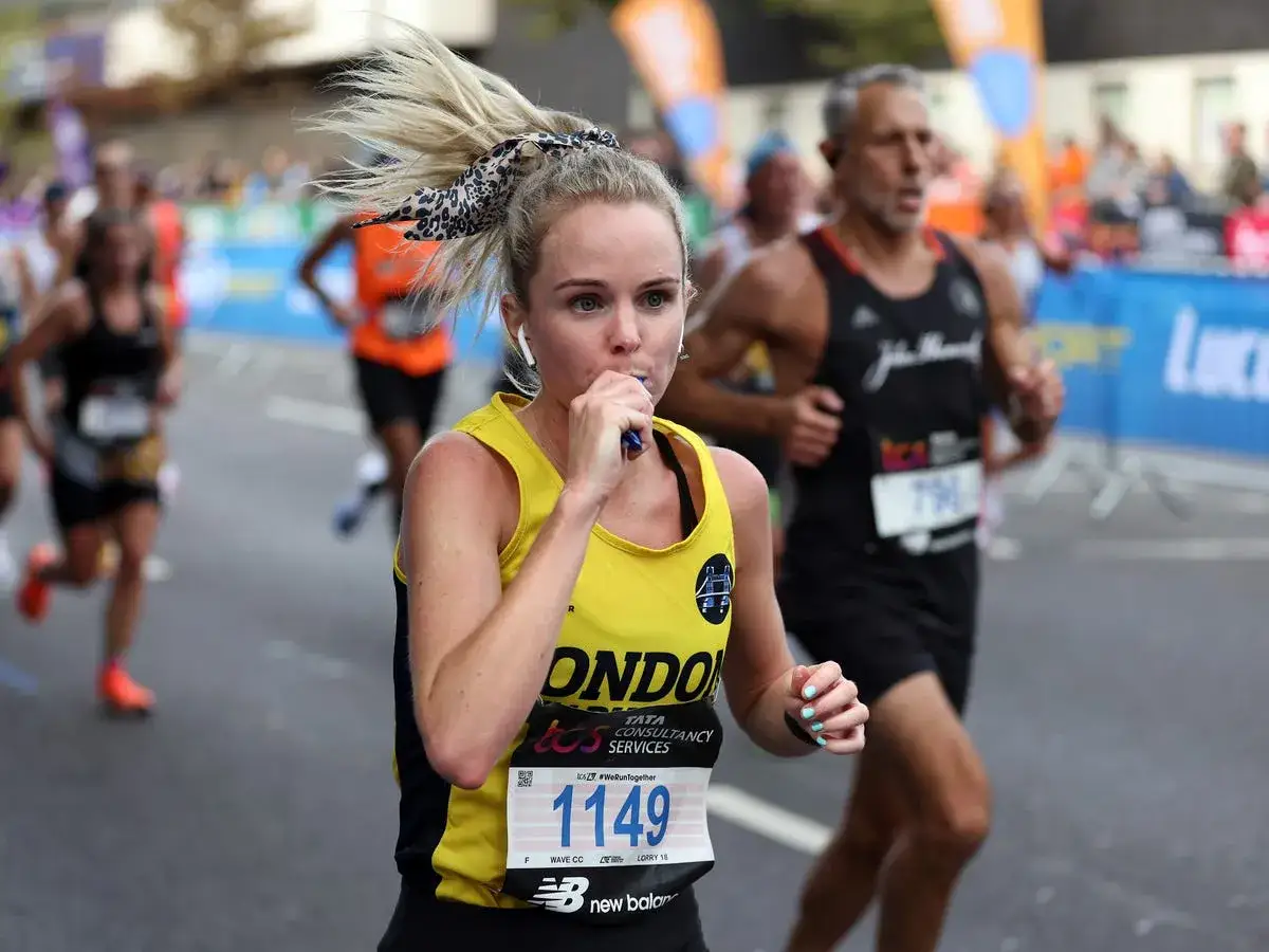 Coureuse de semi-marathon prenant un gel &eacute;nerg&eacute;tique, crucial pour la nutrition pendant l'effort. Cheveux blonds en queue de cheval, dossard 1149.