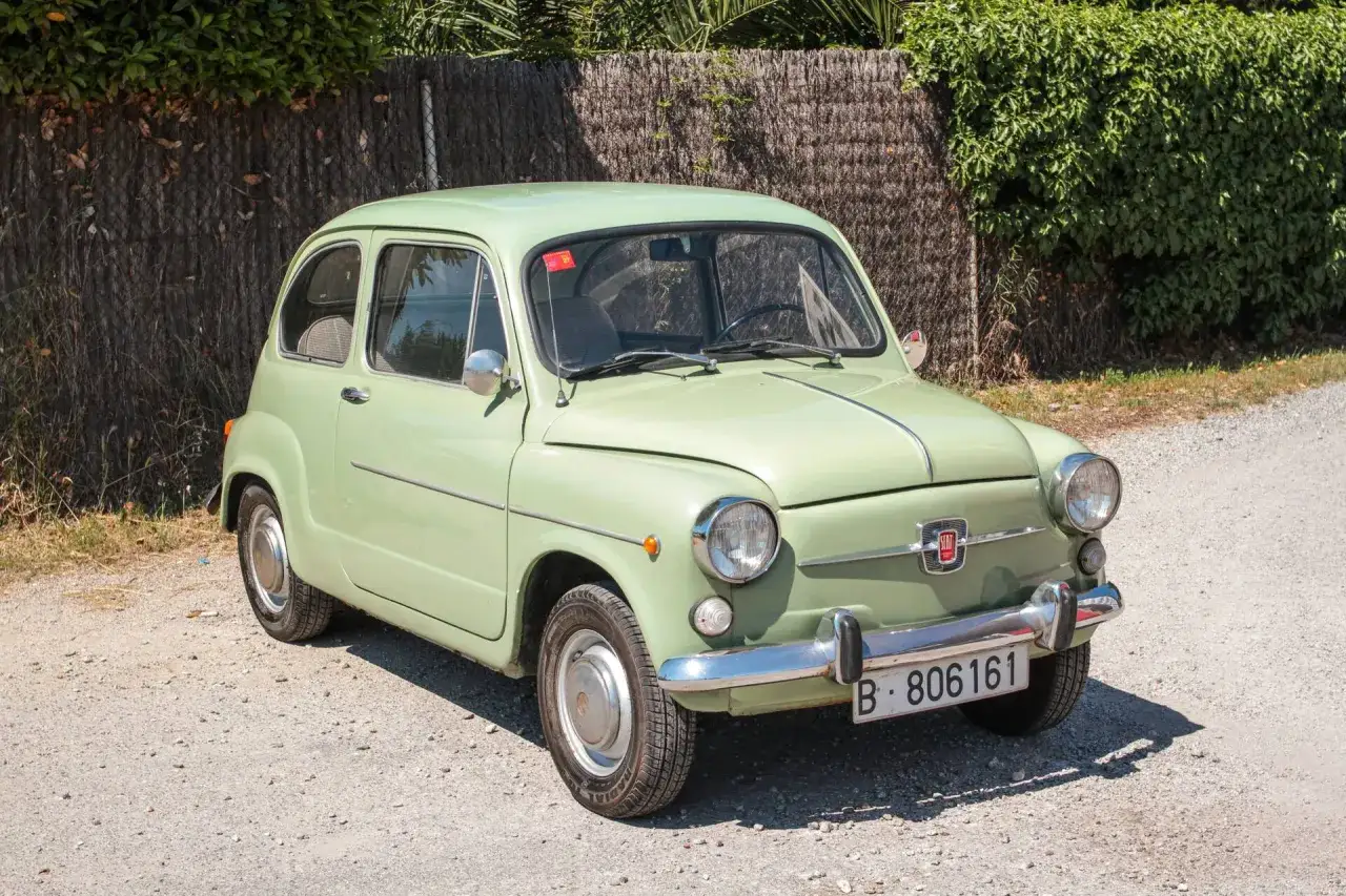 Una Fiat 600 verde pastello, un'icona del design italiano, con il suo logo SEAT che ne attesta l'origine.