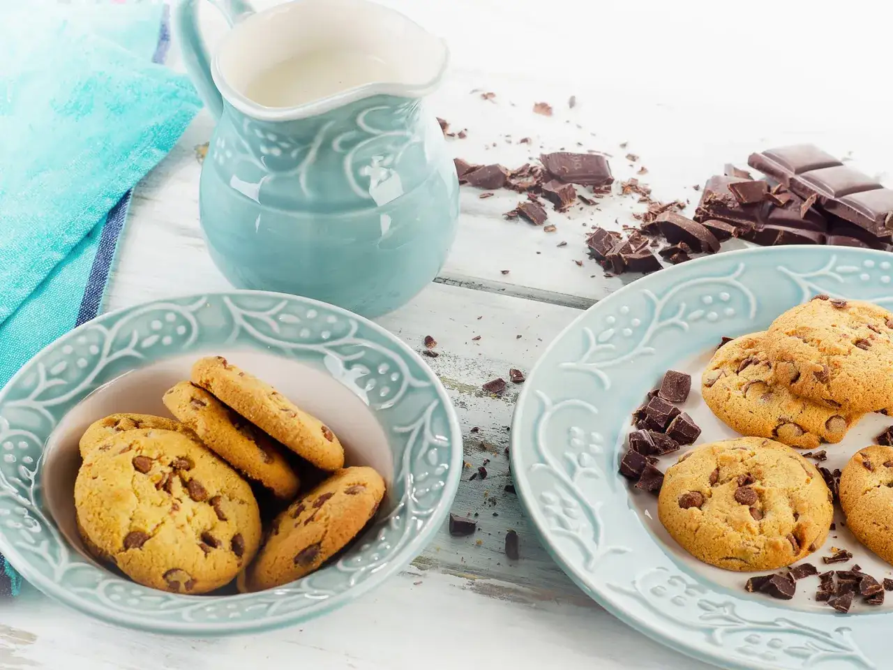 Zwei Teller mit schoko cookies, daneben ein Krug Milch und zerbrochene Schokolade.