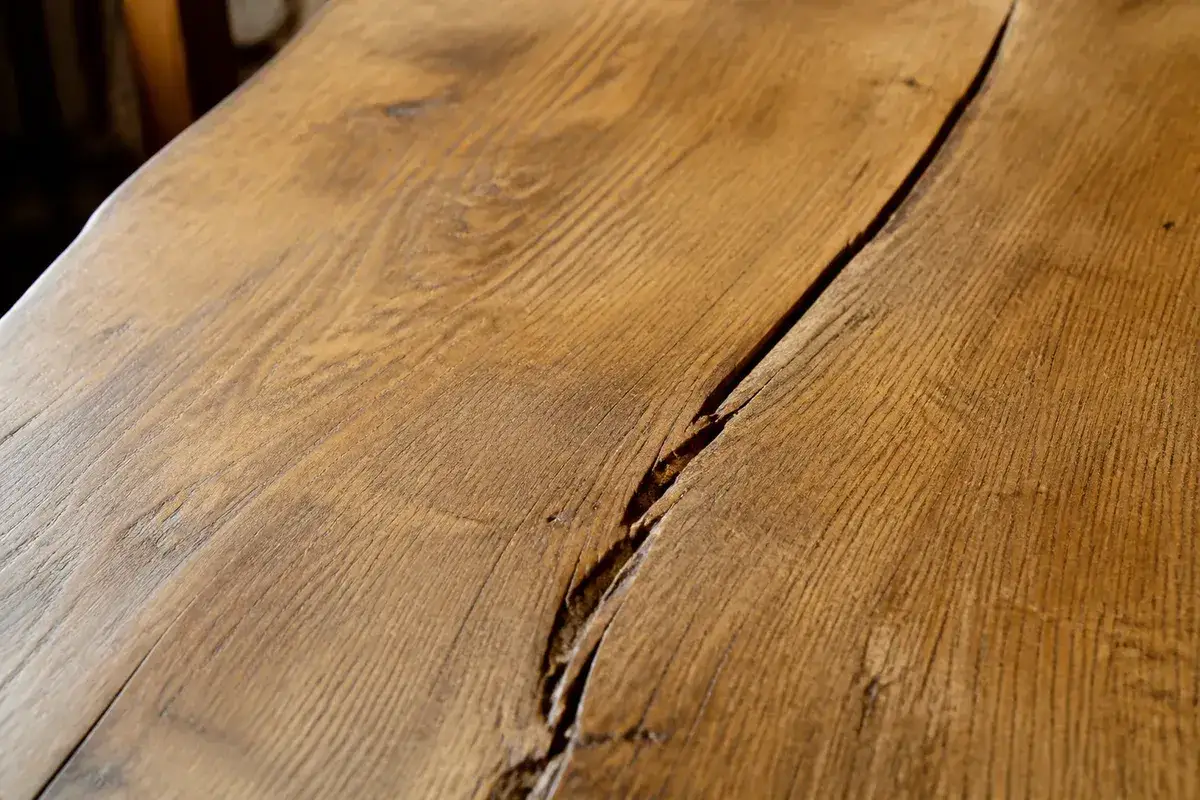 Gros plan sur une table en bois qui se fissure, r&eacute;v&eacute;lant la texture naturelle et les marques du temps.