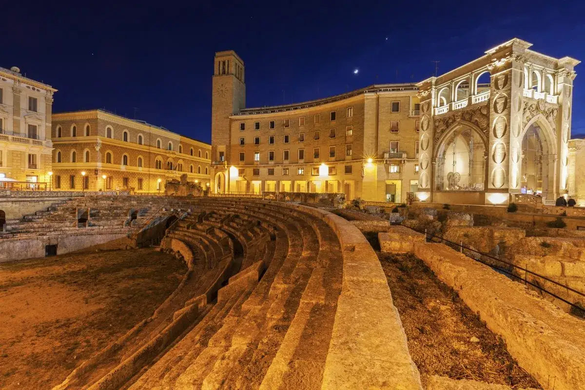L'anfiteatro romano illuminato di notte a Lecce, con edifici storici sullo sfondo. Lecce vale la pena visitarla per la sua bellezza senza tempo.