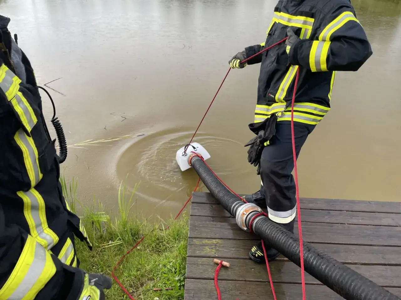 Feuerwehrleute f&uuml;hren eine wasserentnahme offenes gew&auml;sser fwdv 3 durch. Ein Tauchpumpen-Ansaugschlauch wird ins tr&uuml;be Wasser gelassen.