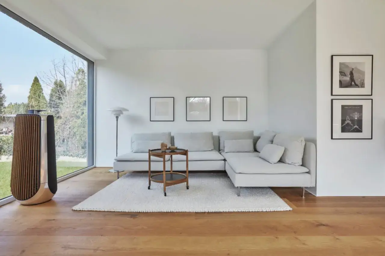 Minimalistisches wohnzimmer gestalten mit großem Fenster, bequemer Couch, Beistelltisch und stilvollem Lautsprecher.