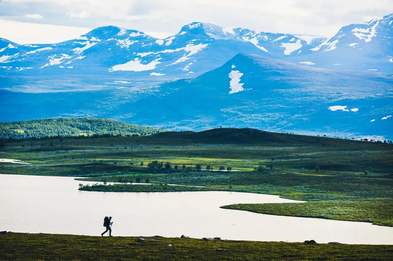 Ensam vandrare med ryggsäck vid en sjö i fjällen, en perfekt sommardag för att vandra Sverige.