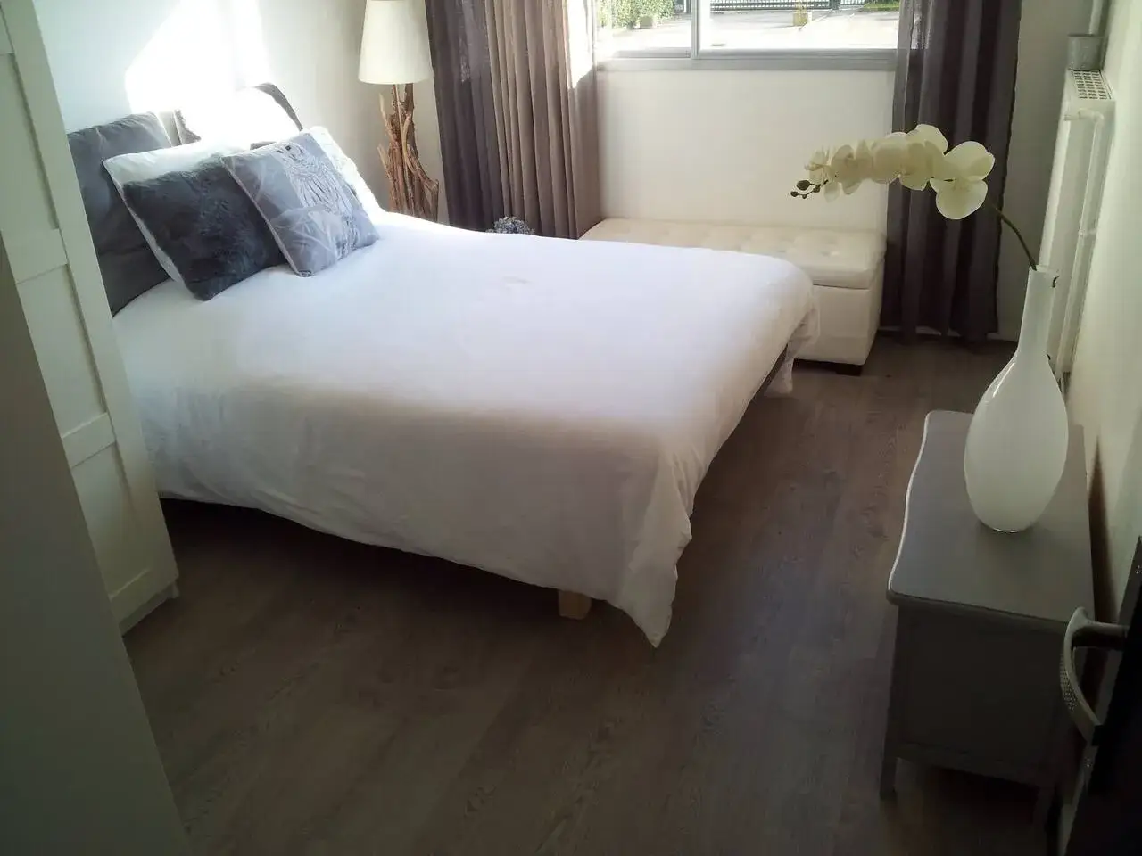Chambre lumineuse avec lit blanc, coussins gris, orchid&eacute;e et vase. Id&eacute;al pour louer une partie de sa r&eacute;sidence principale.
