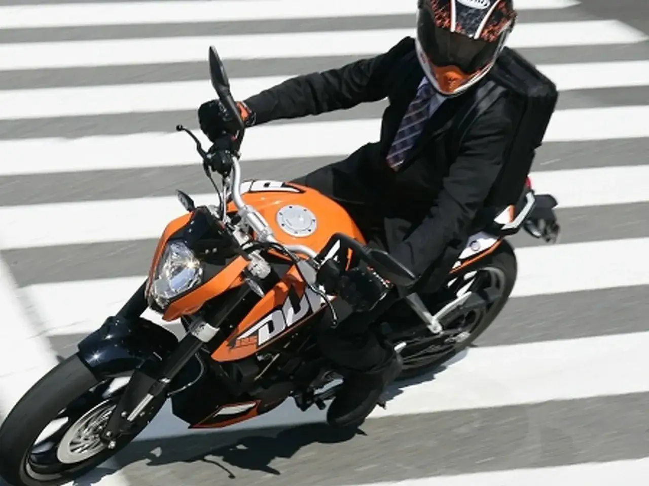 Hombre con traje y casco conduce una KTM Duke 125 naranja. El peso de la moto es ideal para la ciudad.