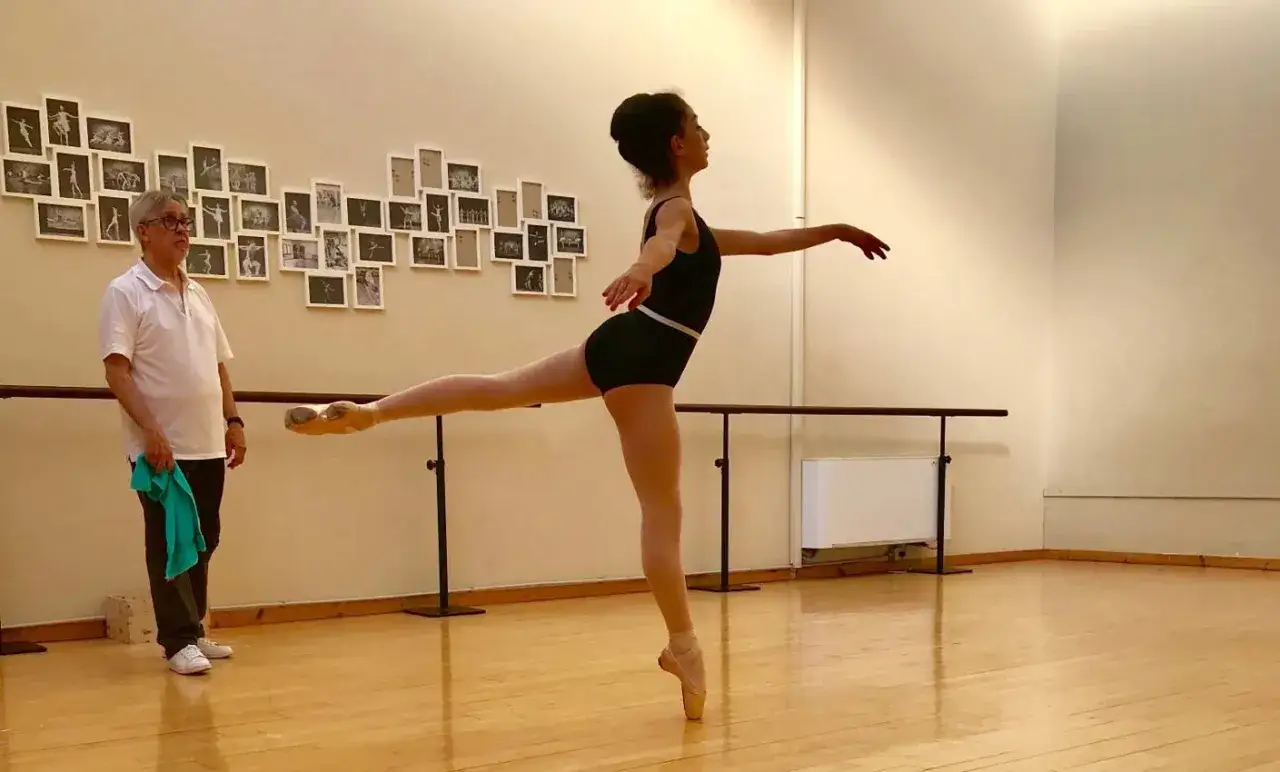 Un maestro osserva una ballerina in posa, un'immagine che cattura l'essenza di cos'è la danza classica: disciplina, grazia e dedizione.