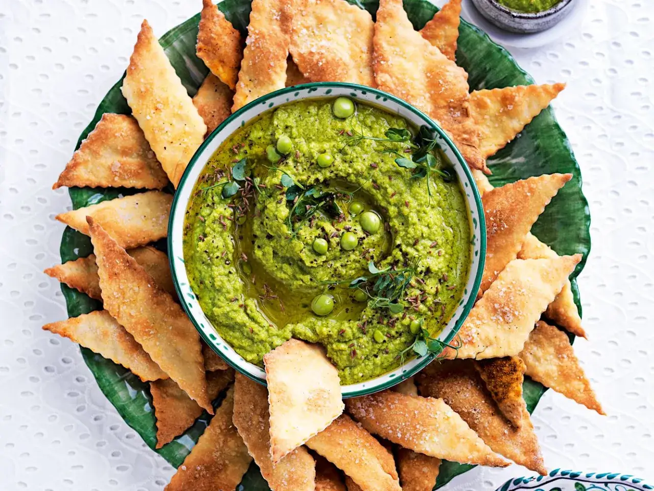 Hummus di piselli cremoso, guarnito con piselli freschi e germogli, servito con croccanti triangoli di pane tostato.