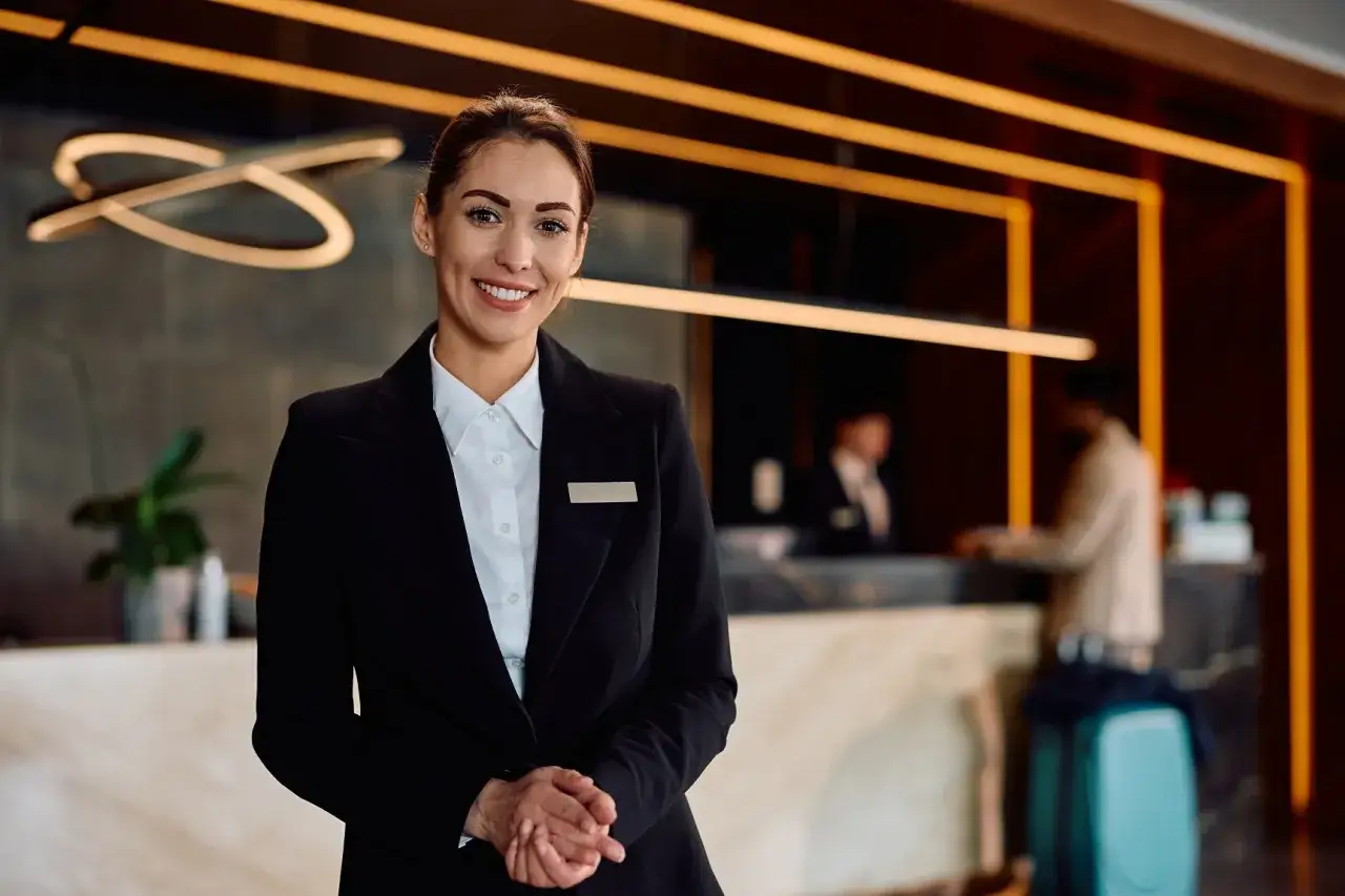 Uśmiechnięta recepcjonistka w eleganckim stroju, symbolizująca profesjonalizm i kompetencje twarde w branży hotelarskiej.